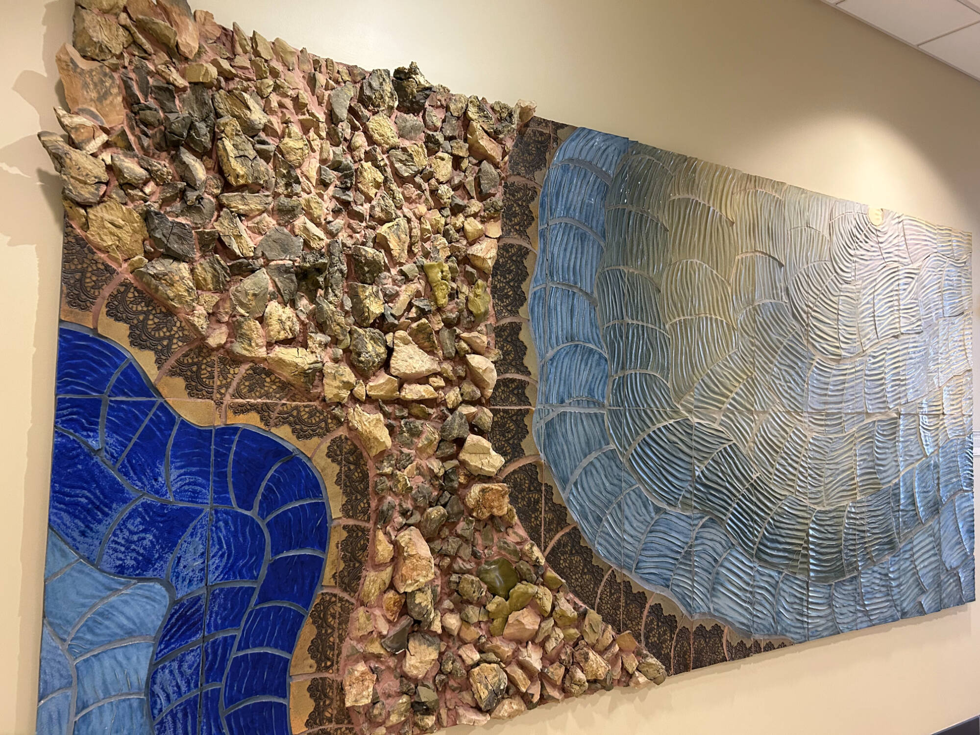 Large mural that looks like a colorful topographic map in shades of blue and brown created with different textured tiles and ceramic pieces.